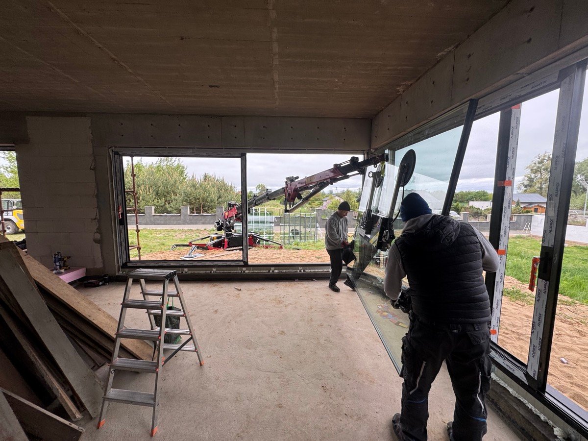 Installers guiding an oversized glass unit fed through the opening by a compact crane